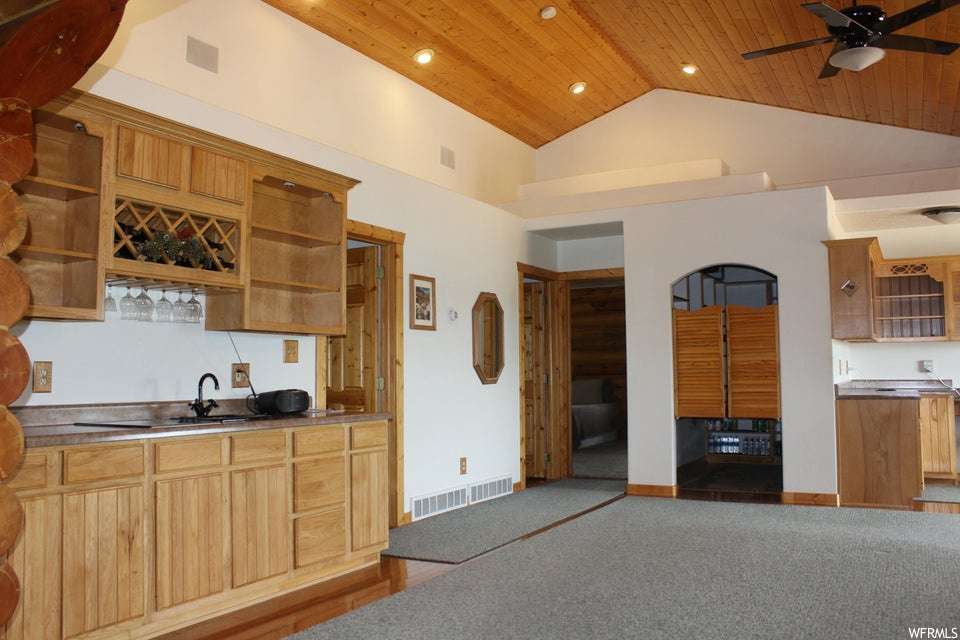 Kitchen with brown cabinets, light carpet, wooden ceiling, ceiling fan, lofted ceiling, and a high ceiling