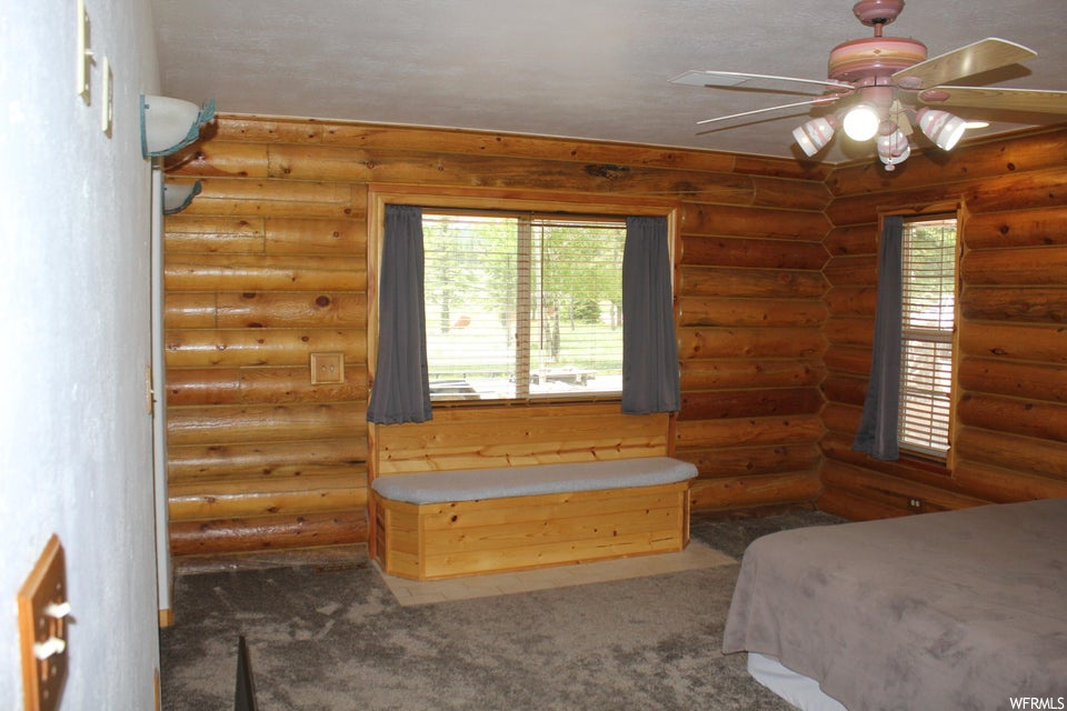 Bedroom featuring log walls, dark carpet, and ceiling fan