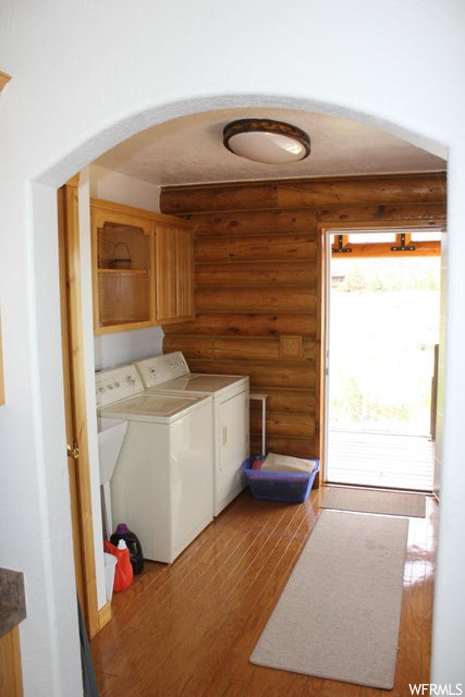 Laundry area featuring separate washer and dryer, light hardwood flooring, and log walls