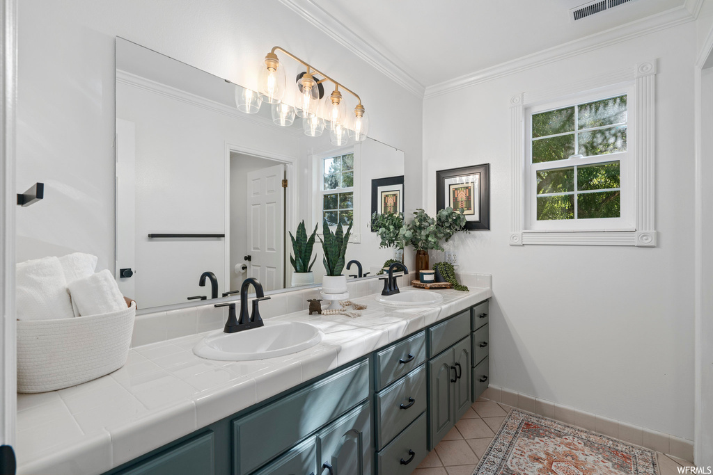 Bathroom featuring crown molding, dual bowl vanity, light tile flooring, and mirror