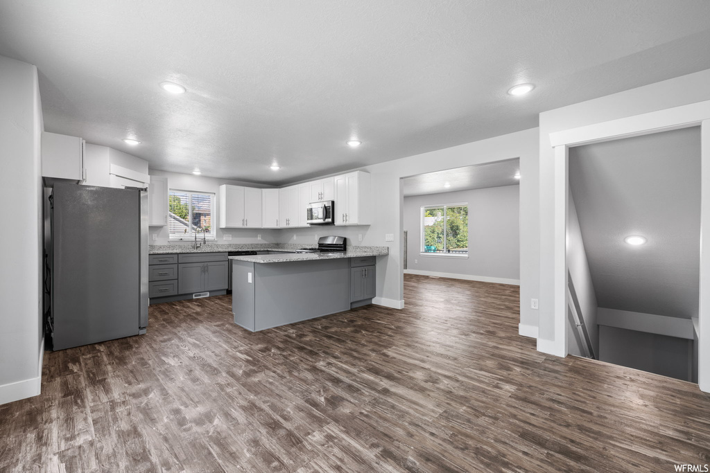 Kitchen featuring white cabinets, light countertops, a healthy amount of sunlight, appliances with stainless steel finishes, and dark hardwood flooring