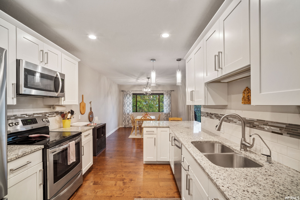 Kitchen featuring pendant lighting, light hardwood flooring, white cabinets, backsplash, and sink