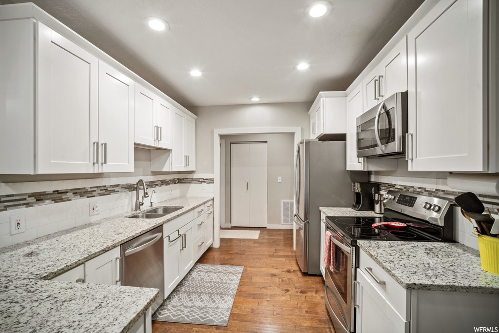 Kitchen featuring white cabinets, sink, light hardwood flooring, and appliances with stainless steel finishes