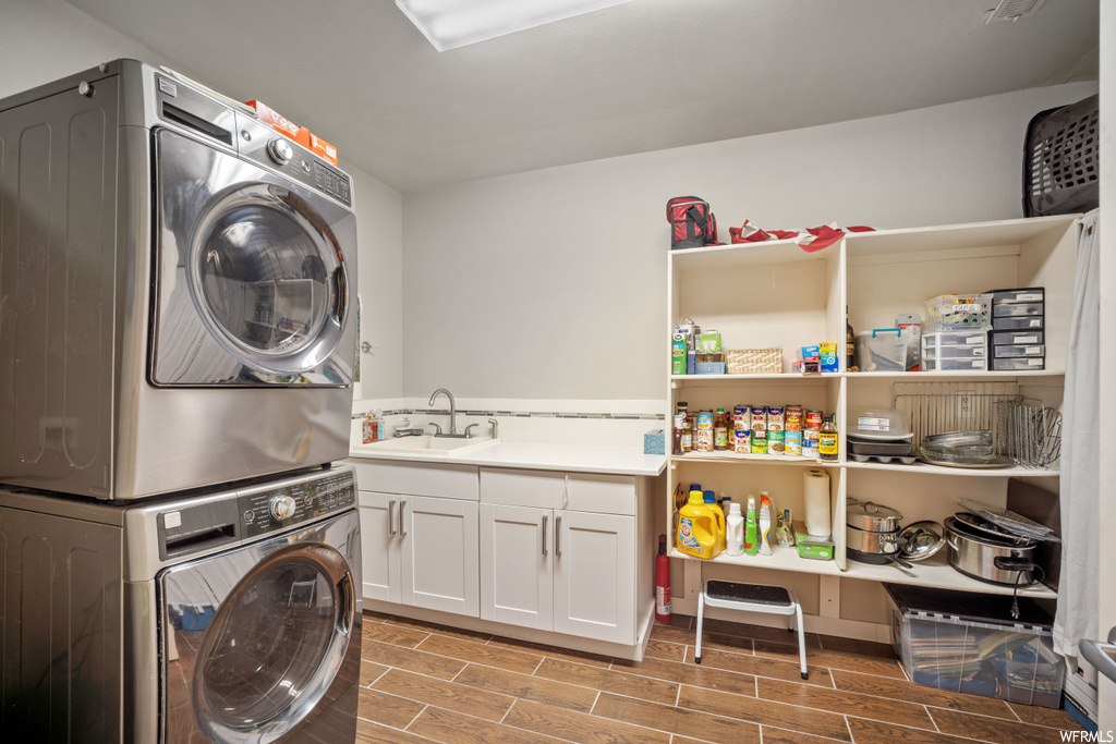 Laundry room featuring cabinets, stacked washer and dryer, and sink