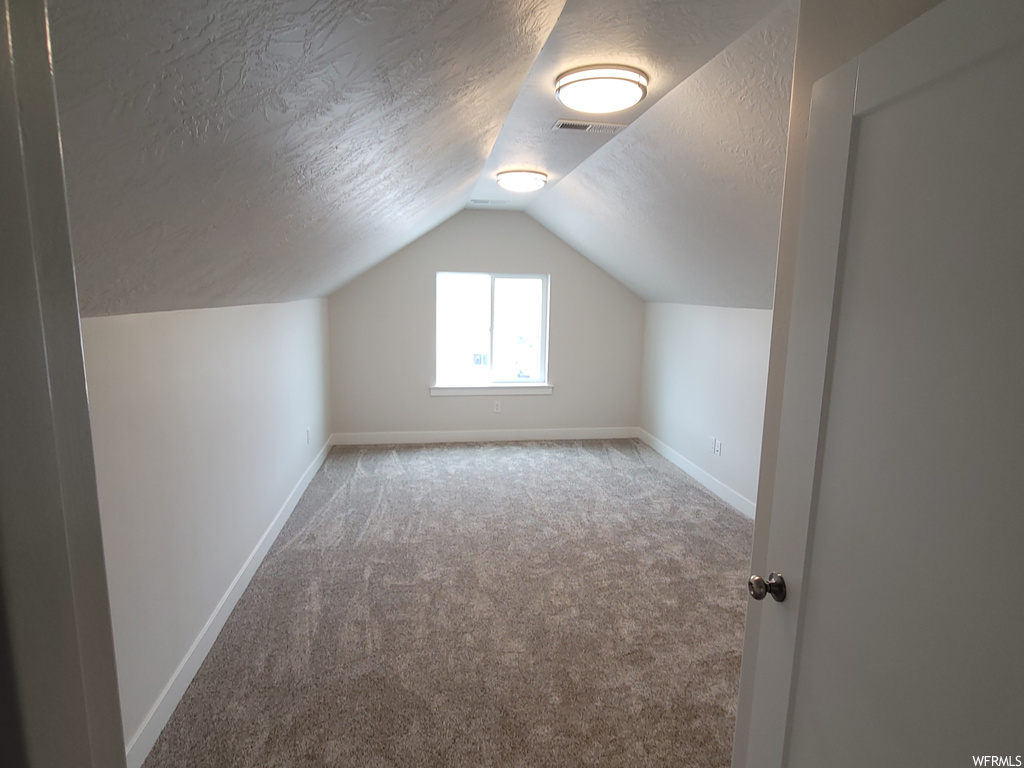 Bonus room featuring light carpet, vaulted ceiling, and a textured ceiling