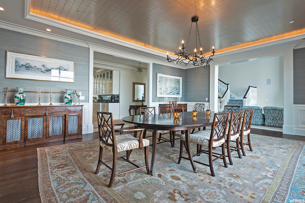 Wood floored dining space featuring crown molding, a chandelier, and a tray ceiling