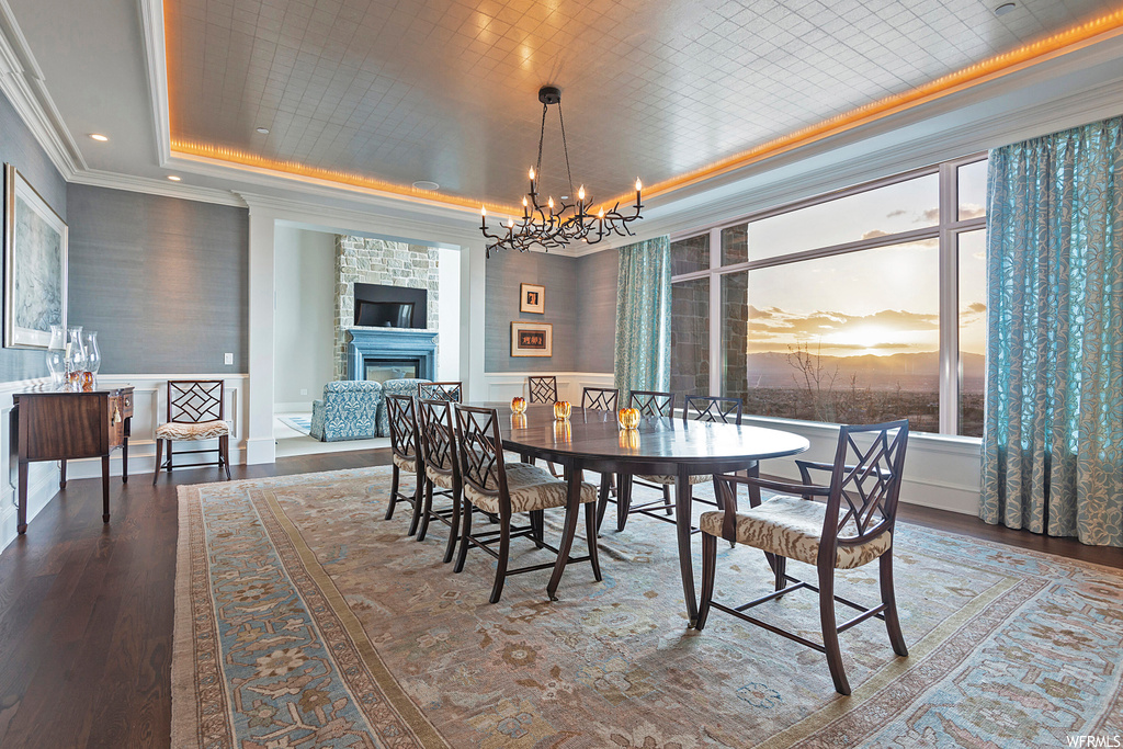 Wood floored dining room featuring crown molding, a chandelier, a fireplace, and a raised ceiling
