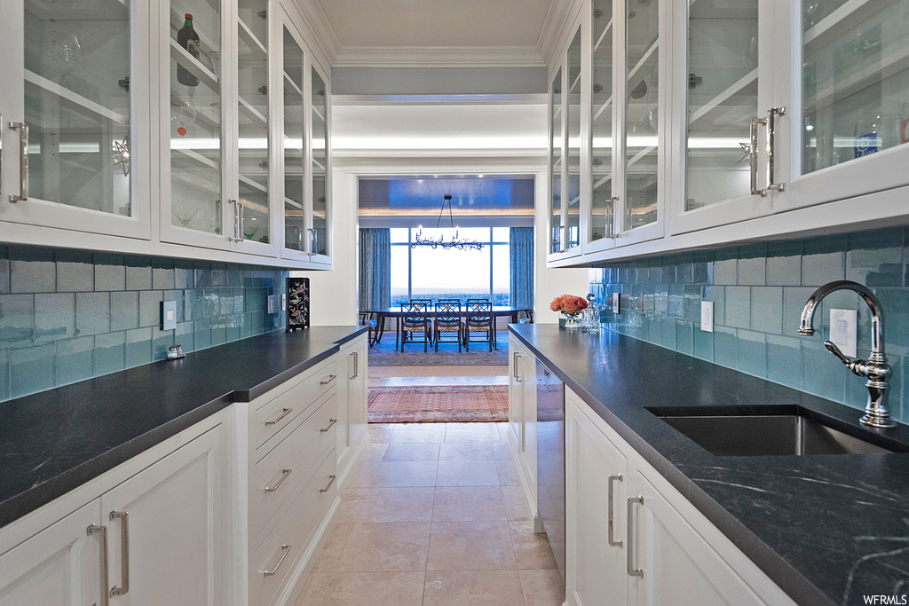 Kitchen featuring ornamental molding, backsplash, white cabinets, light tile floors, and dark countertops