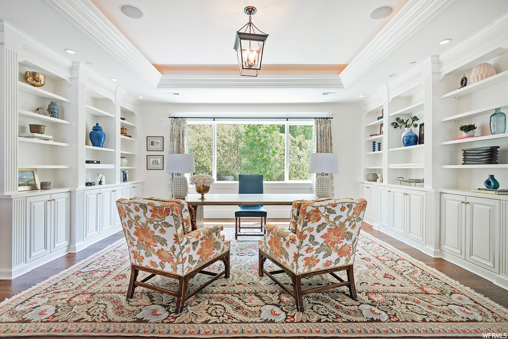 Wood floored home office with built in features, ornamental molding, and a raised ceiling