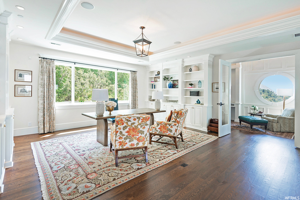 Hardwood floored office featuring ornamental molding, built in shelves, and a raised ceiling