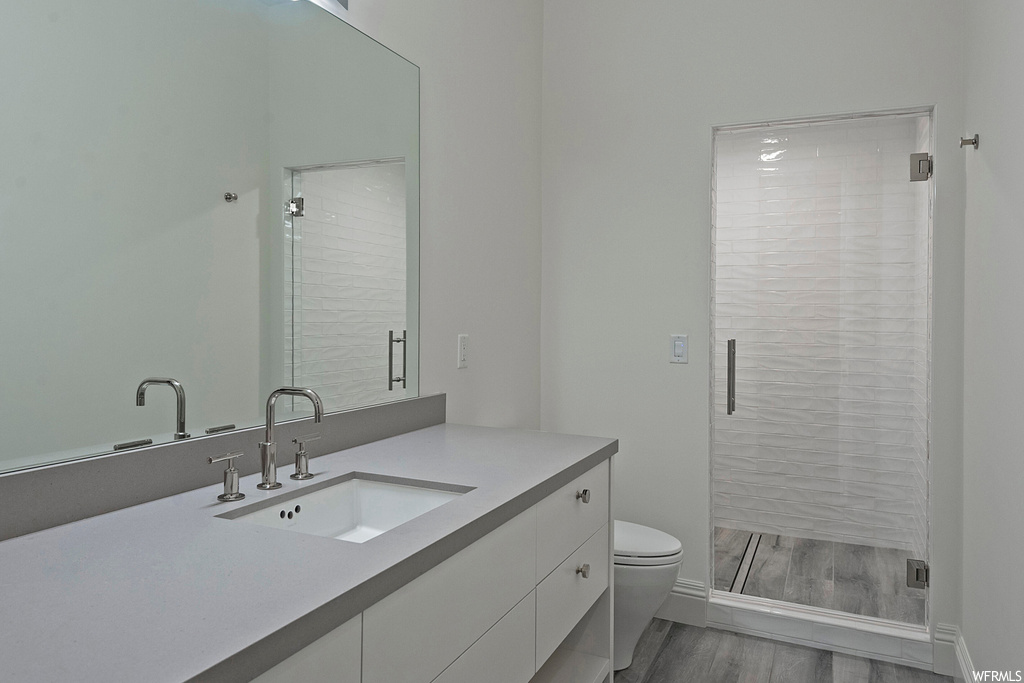 Bathroom featuring hardwood floors, vanity, mirror, and a tile shower