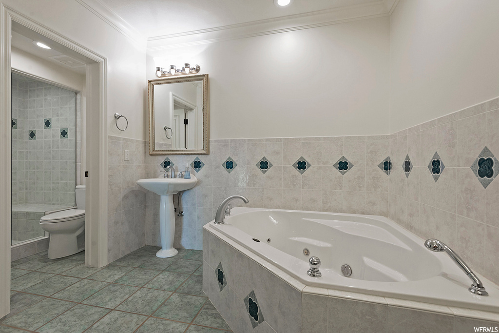 Full bathroom featuring crown molding, light tile flooring, mirror, sink, tile walls, and shower with separate bathtub