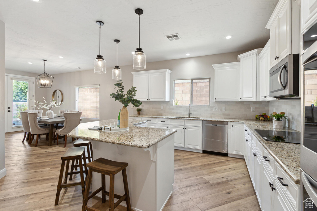 Kitchen featuring hanging light fixtures, light hardwood / wood-style floors, tasteful backsplash, and stainless steel appliances