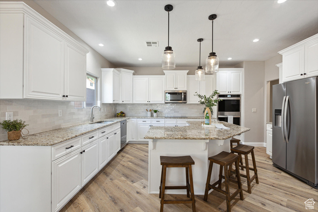 Kitchen with white cabinets, backsplash, appliances with stainless steel finishes, and light hardwood / wood-style floors