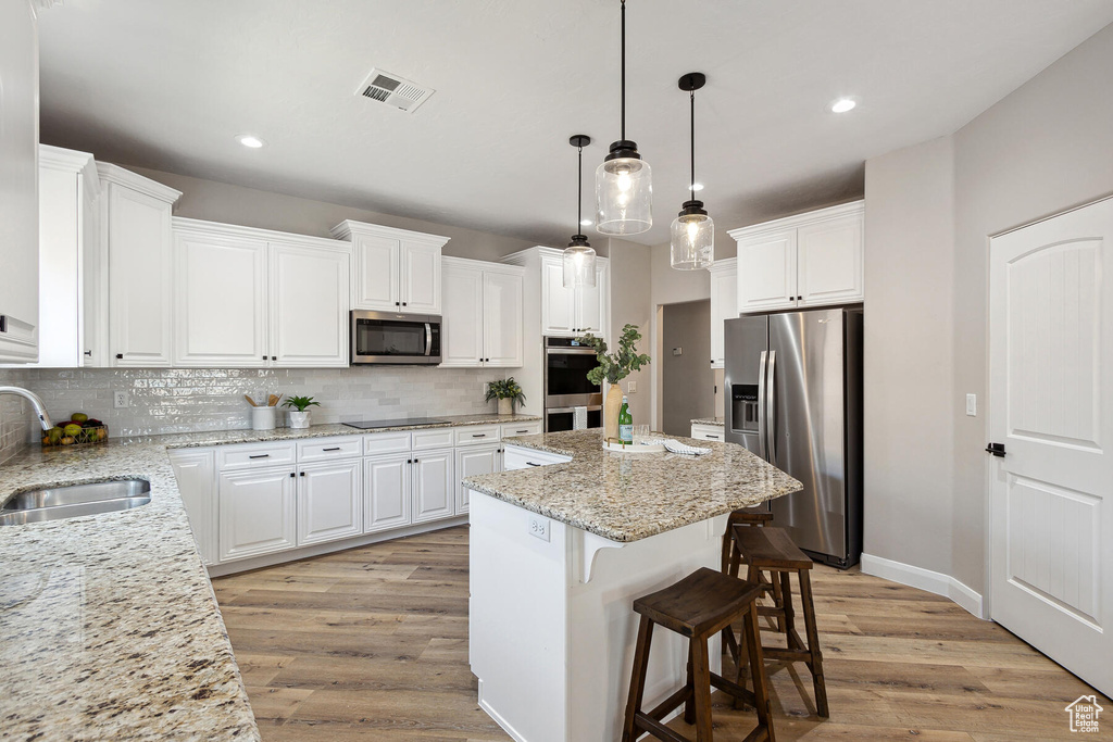 Kitchen featuring stainless steel appliances, sink, light hardwood / wood-style floors, white cabinetry, and a kitchen island