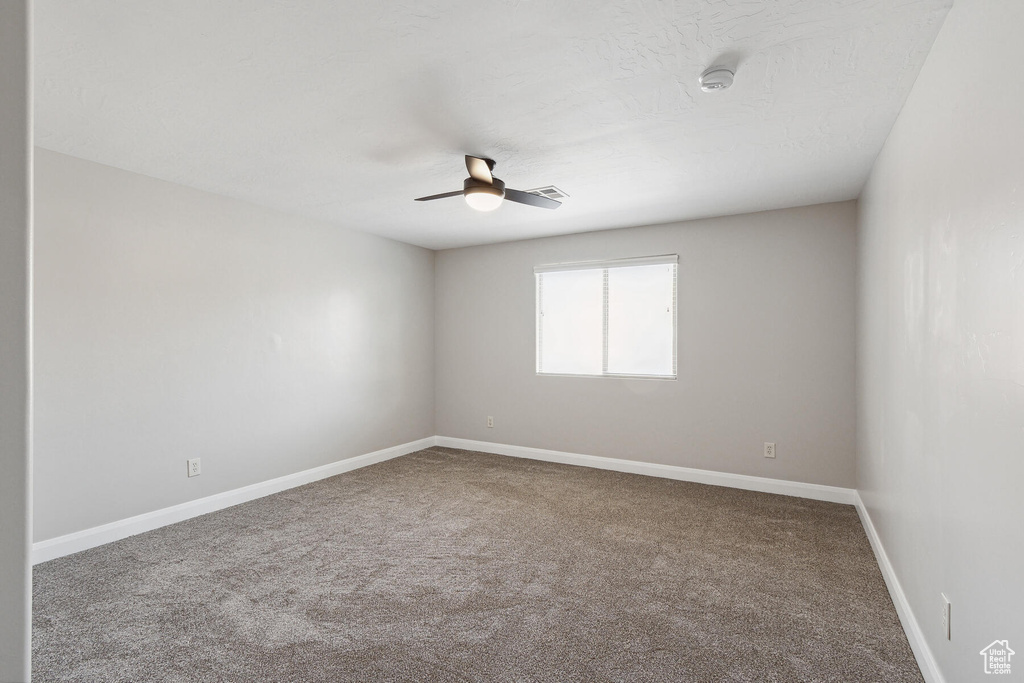 Empty room with ceiling fan and dark carpet