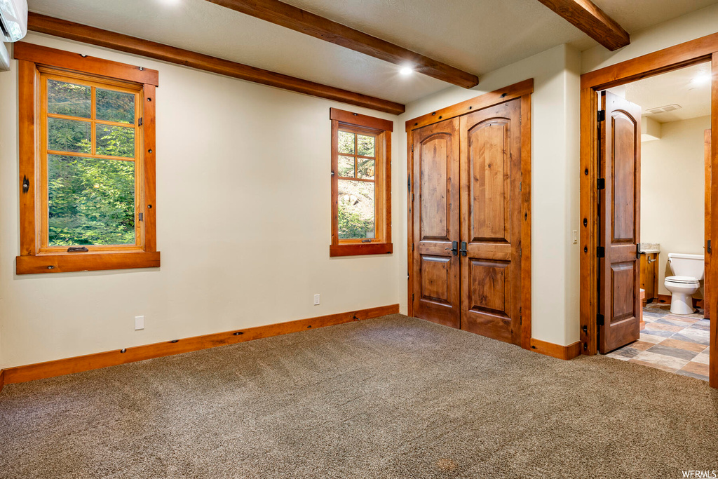 Carpeted bedroom featuring beam ceiling and multiple windows