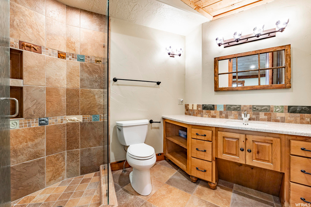Bathroom with vanity, a shower with door, tile walls, backsplash, and light tile floors