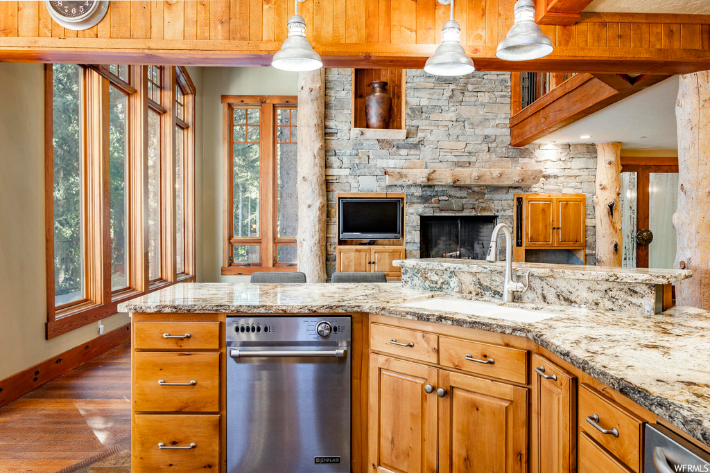 Kitchen featuring brown cabinets, dishwasher, hardwood flooring, light stone countertops, and pendant lighting