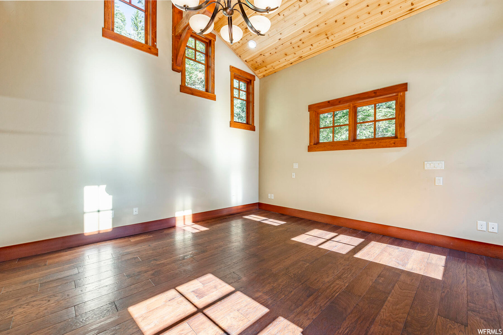 Spare room featuring a notable chandelier, vaulted ceiling, wooden ceiling, hardwood floors, and a high ceiling