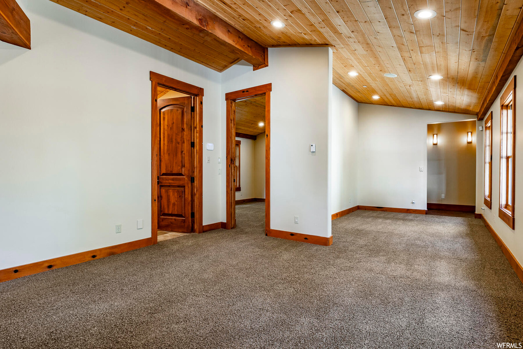 Empty room with vaulted ceiling with beams, light carpet, and wooden ceiling