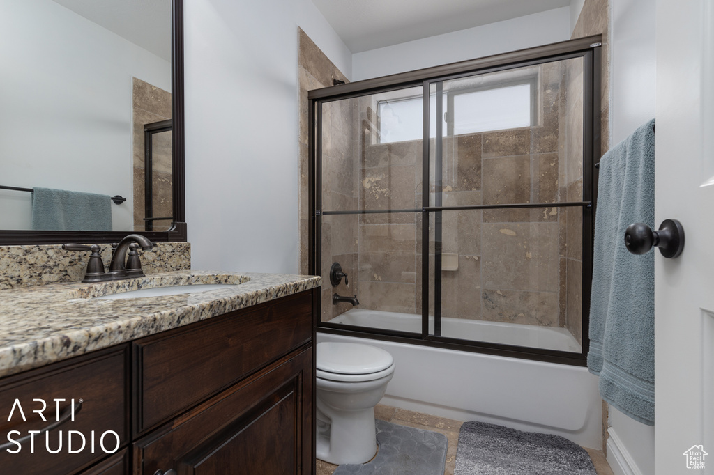 Full bathroom featuring tile flooring, bath / shower combo with glass door, toilet, and large vanity