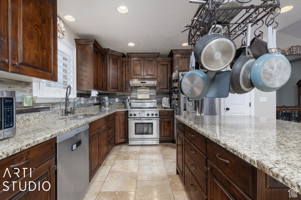 Kitchen featuring stainless steel appliances, light stone counters, light tile floors, backsplash, and dark brown cabinets