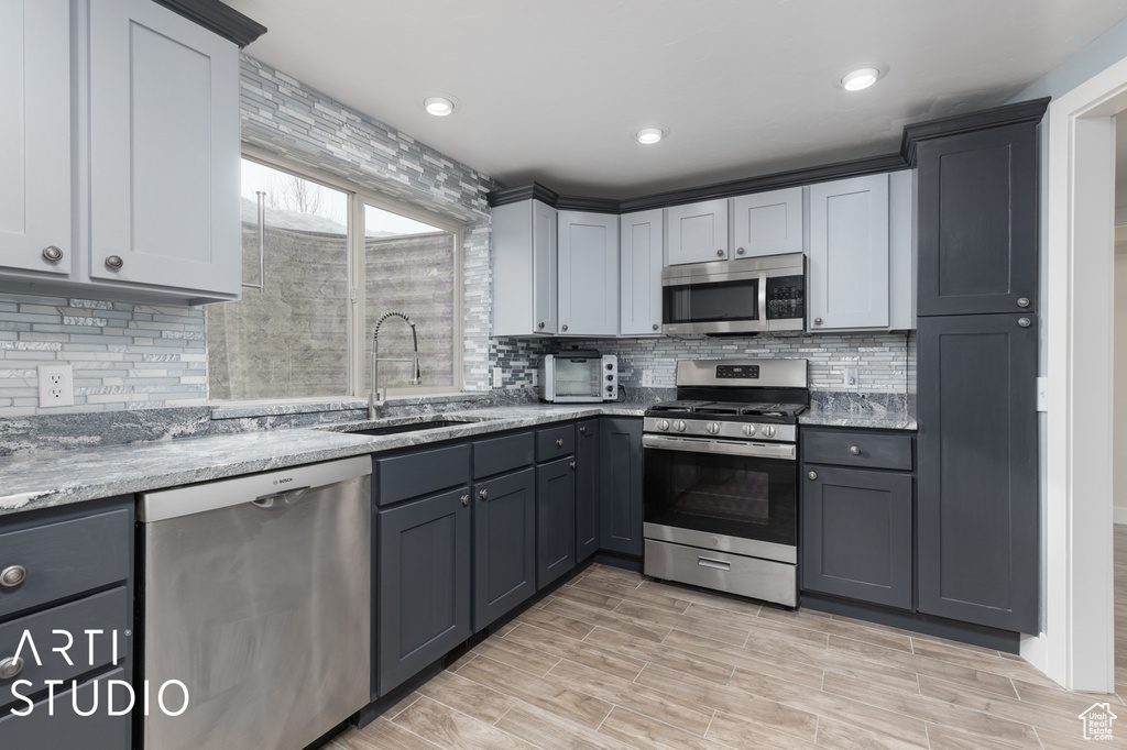 Kitchen featuring tasteful backsplash, gray cabinets, light stone countertops, appliances with stainless steel finishes, and sink