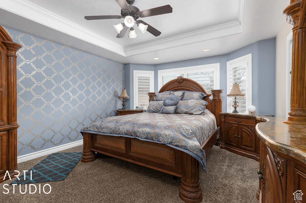 Bedroom with ornamental molding, dark carpet, a tray ceiling, and ceiling fan