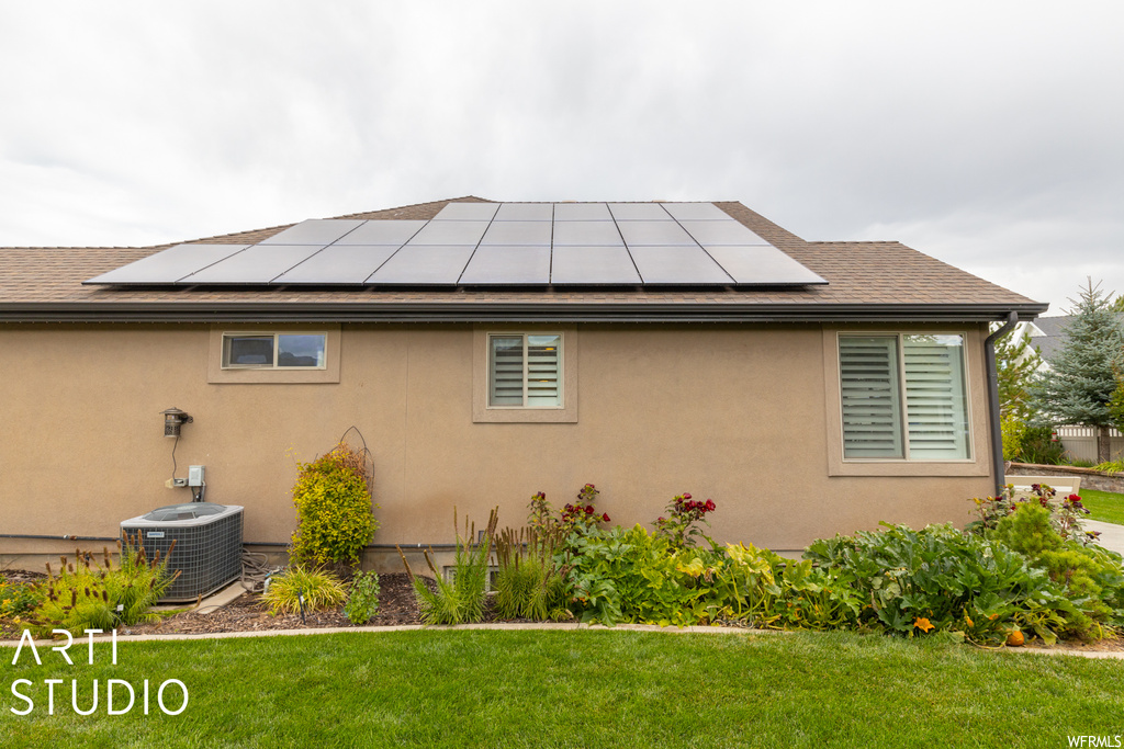 Rear view of house with a yard, central AC, and solar panels