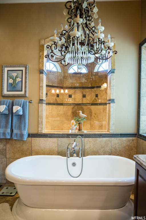 Bathroom with vanity, plenty of natural light, a chandelier, a tub, and tile walls
