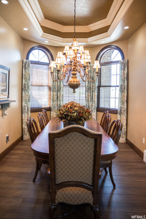 Dining area featuring dark hardwood floors, a tray ceiling, a chandelier, and crown molding