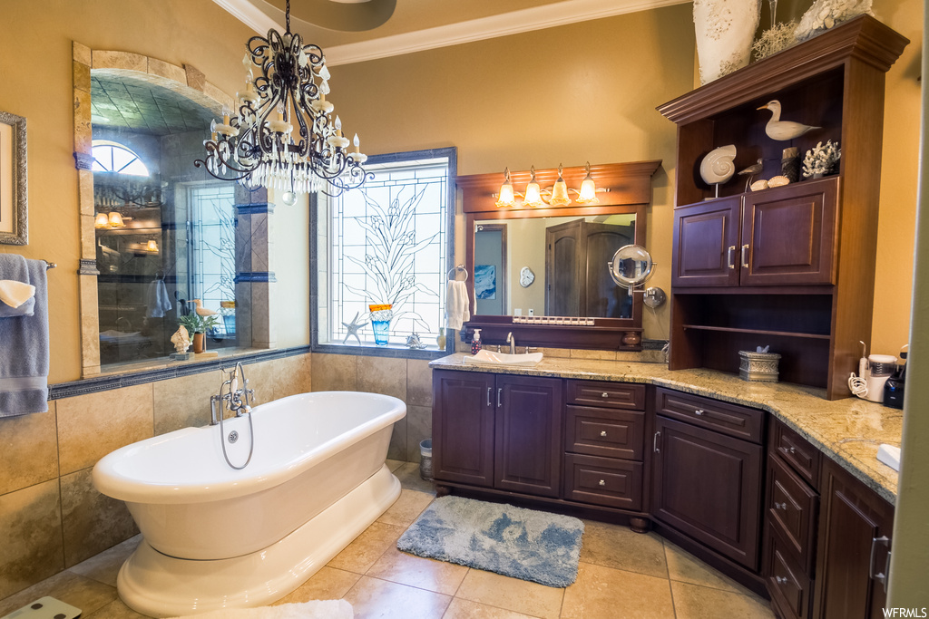 Bathroom featuring mirror, a chandelier, independent shower and bath, light tile floors, crown molding, tile walls, and dual vanity