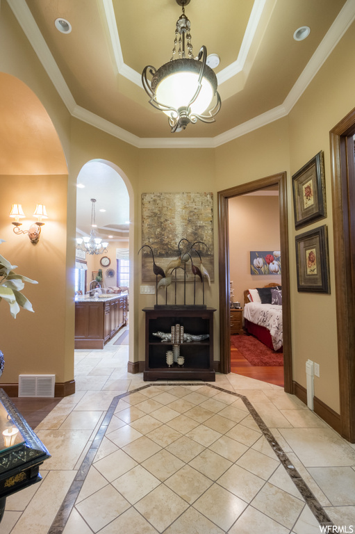 Hallway with a tray ceiling, crown molding, and light tile floors