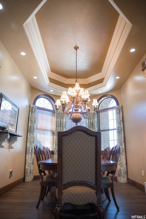 Wood floored dining area featuring a notable chandelier, ornamental molding, and a tray ceiling