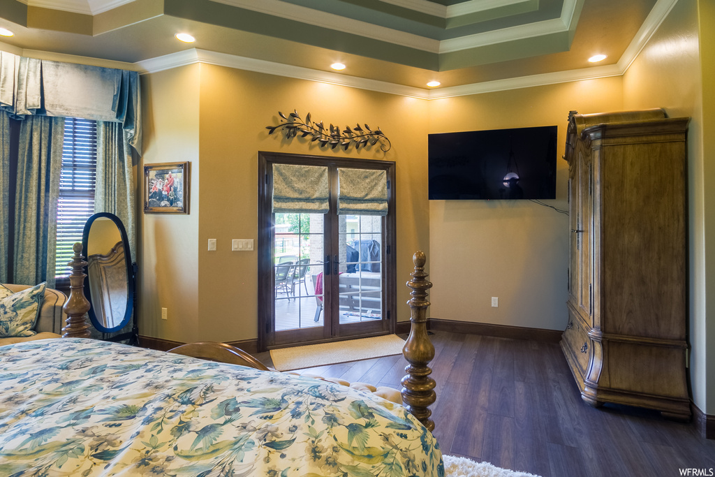 Hardwood floored bedroom featuring a tray ceiling, ornamental molding, and french doors