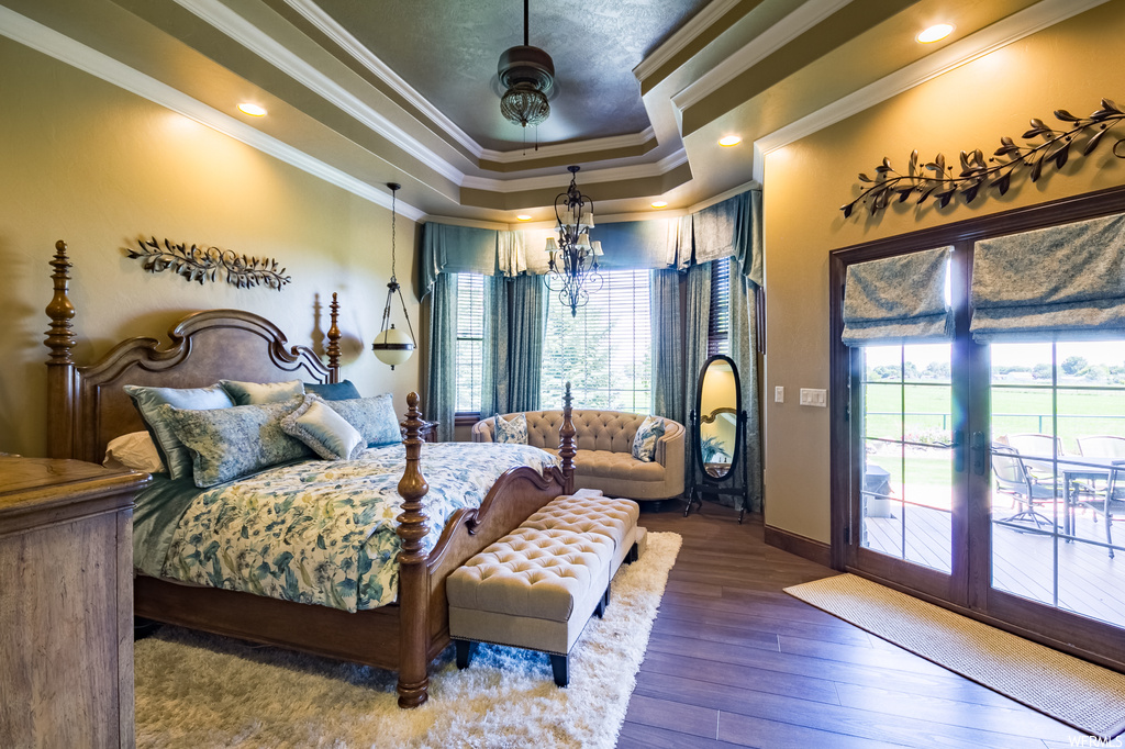 Hardwood floored bedroom with crown molding, a chandelier, multiple windows, and a tray ceiling