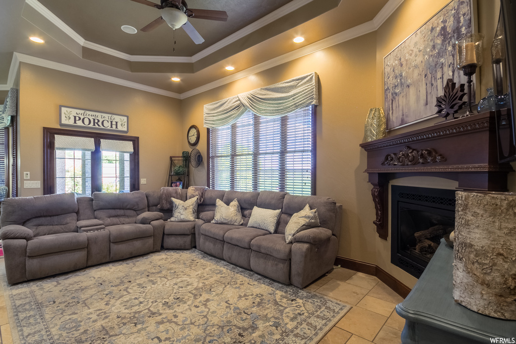 Living room featuring ornamental molding, a tray ceiling, light tile floors, ceiling fan, and a fireplace