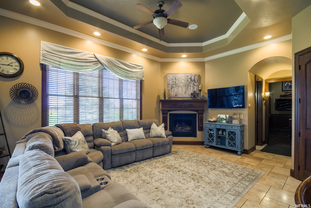 Tiled living room with a tray ceiling, a fireplace, crown molding, and ceiling fan