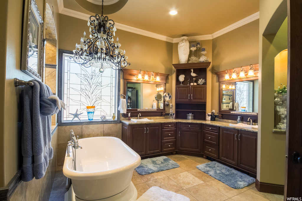 Bathroom featuring a bathing tub, mirror, a chandelier, light tile floors, crown molding, tile walls, and double large vanity