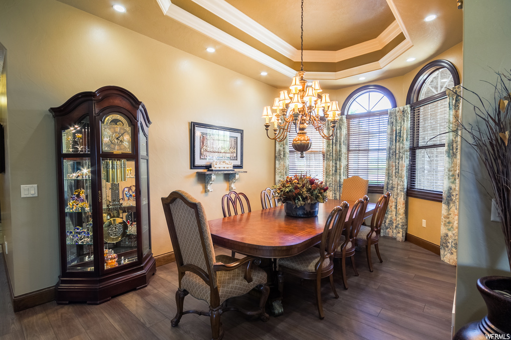 Dining area with a notable chandelier, a raised ceiling, crown molding, and dark hardwood flooring