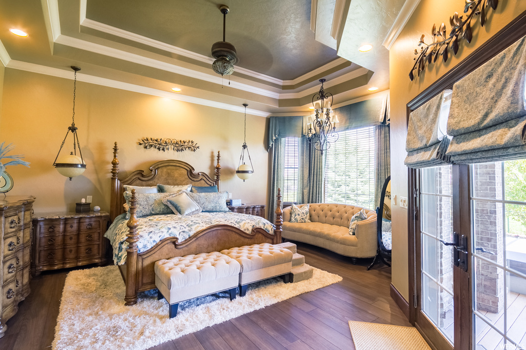 Hardwood floored bedroom with a chandelier, ornamental molding, french doors, and a raised ceiling