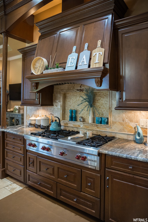 Kitchen featuring light tile floors, backsplash, stainless steel gas stovetop, and dark brown cabinetry