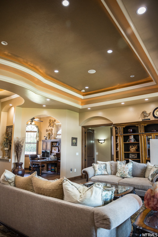 Living room with ceiling fan, ornamental molding, and a raised ceiling