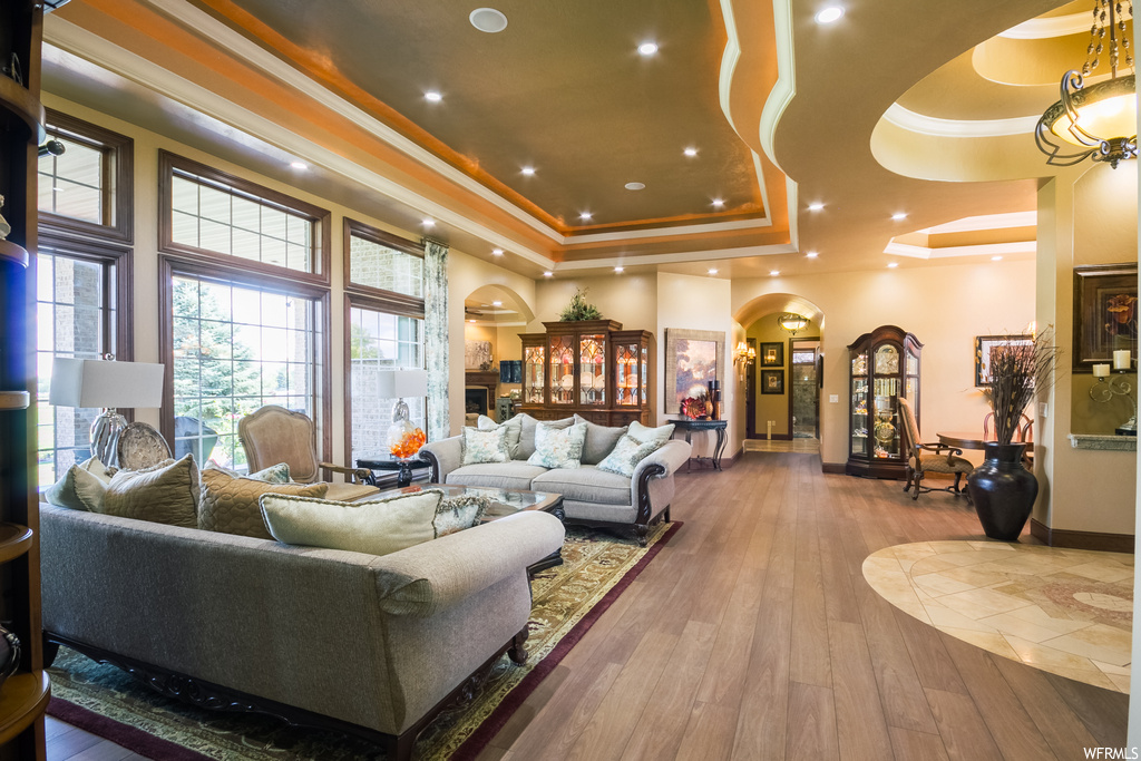 Living room featuring ornamental molding, a tray ceiling, a high ceiling, and light hardwood flooring