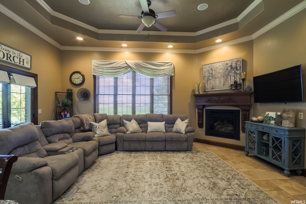 Tiled living room featuring ornamental molding, a tray ceiling, a fireplace, and ceiling fan