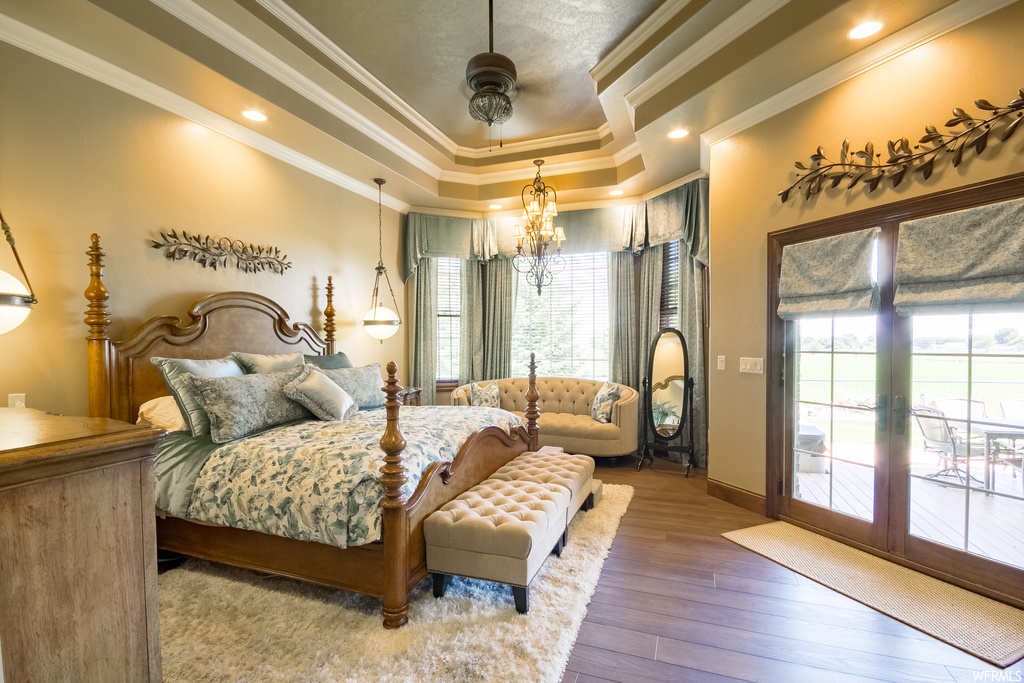 Hardwood floored bedroom with a chandelier, ornamental molding, and a tray ceiling