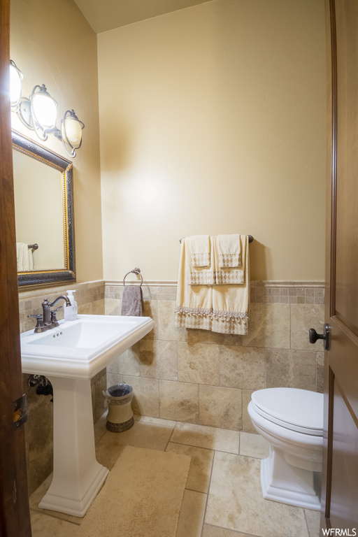 Bathroom with tile walls, washbasin, mirror, and light tile floors
