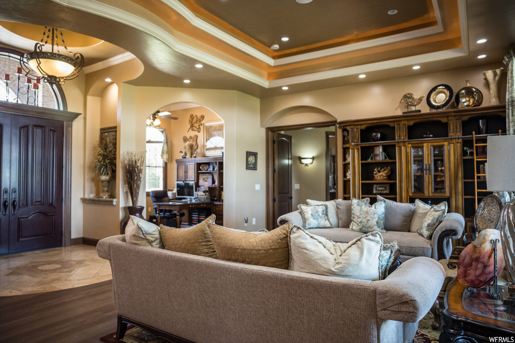 Living room featuring a tray ceiling, tile floors, and crown molding
