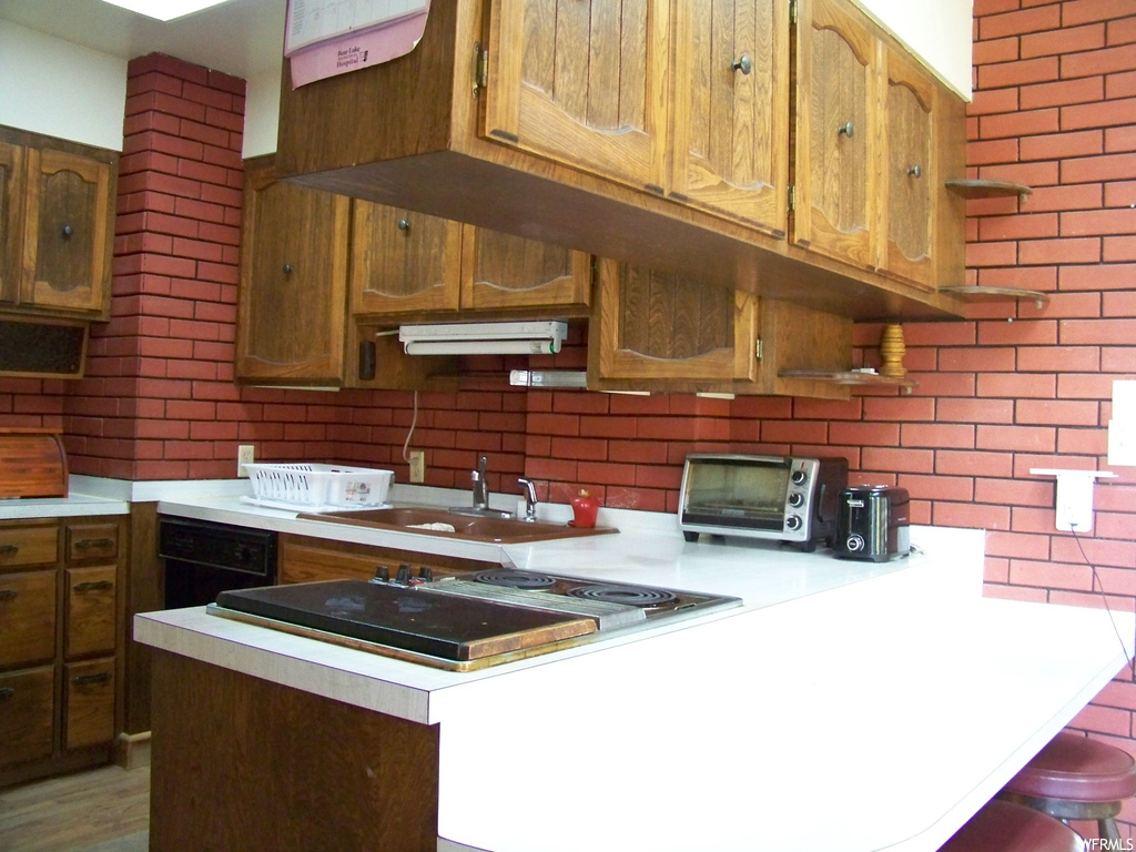 Kitchen featuring light countertops, light hardwood flooring, brick wall, and brown cabinets